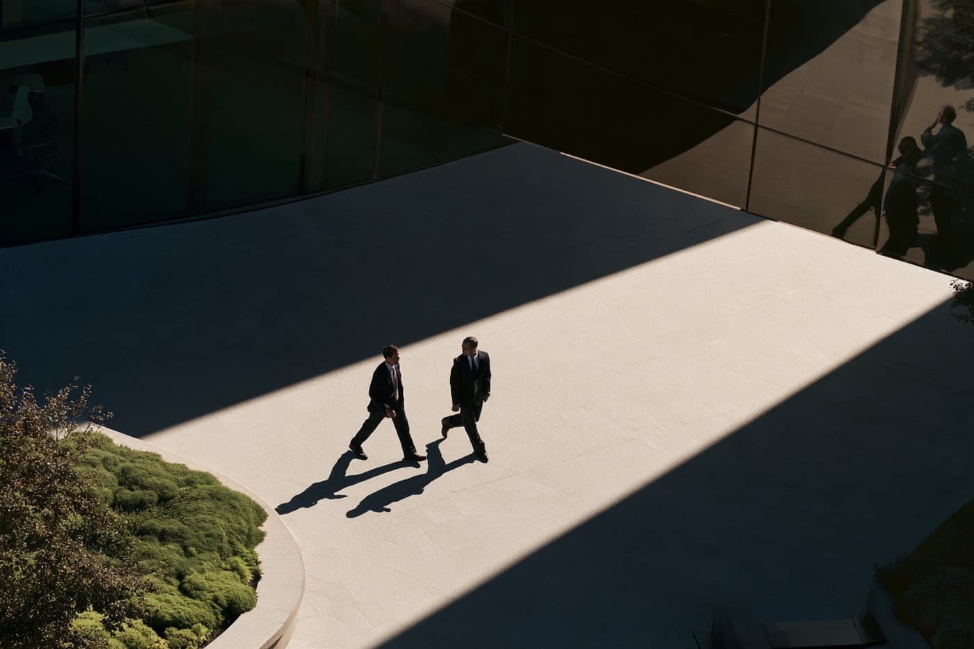 Two colleagues crossing a sunlit plaza outside an office building.